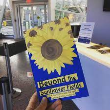 photo of zine cover: hand holding a blue zine with sunflowers on it. Title in blue with tangerine background