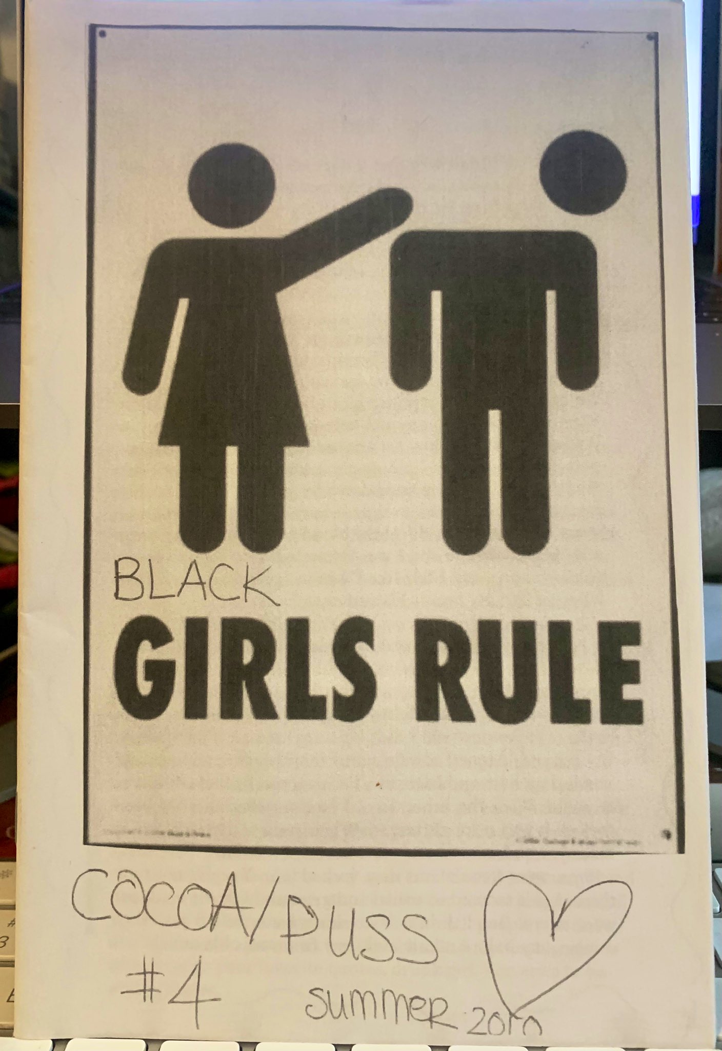 Graphic of stick figure bathroom woman flicking off stick figure bathroom man’s head.  Cocoa/Puss no. 4: Black Girls Rule by LaMesha summer 2010